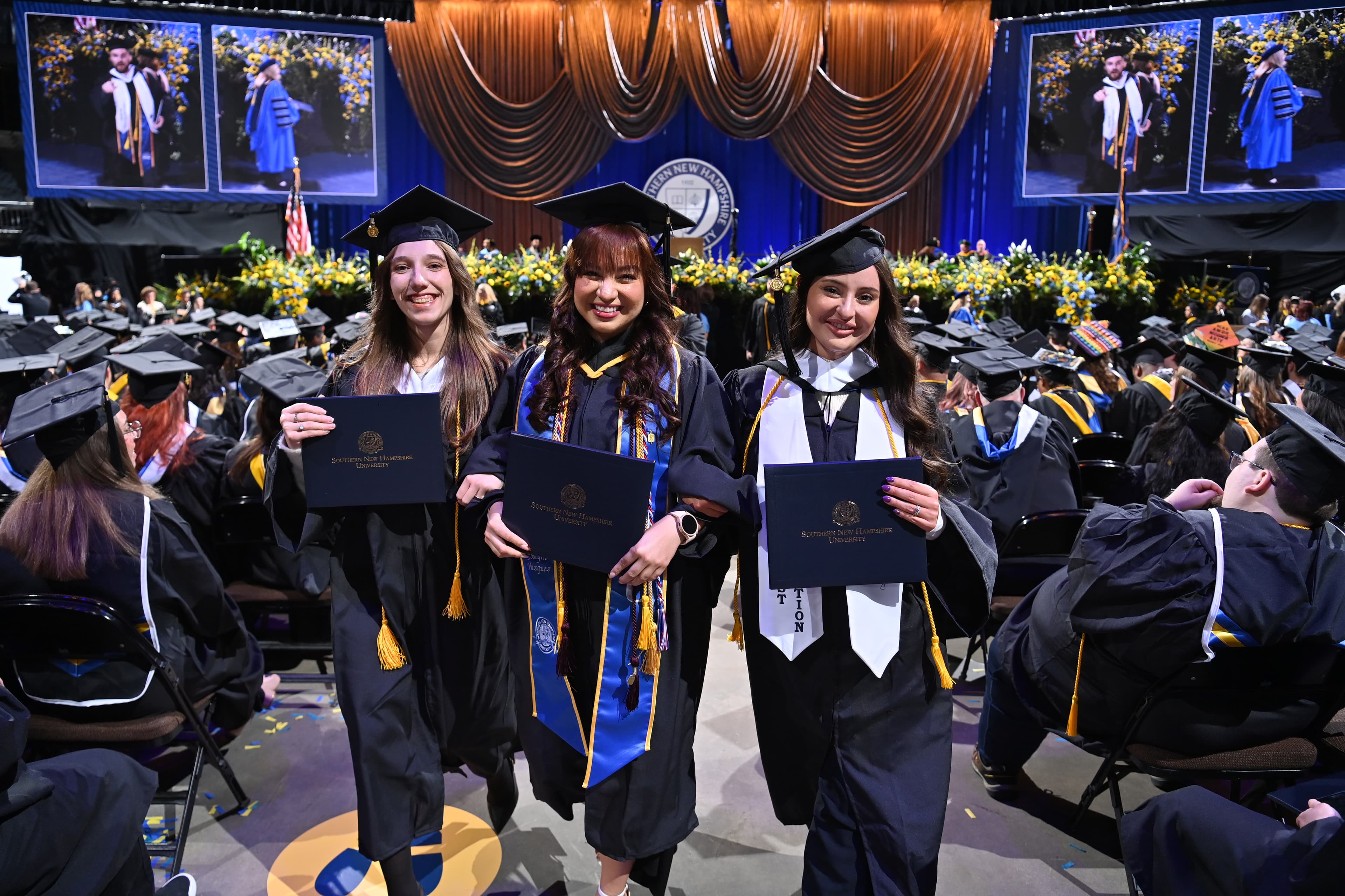Three SNHU graduates in academic regalia
